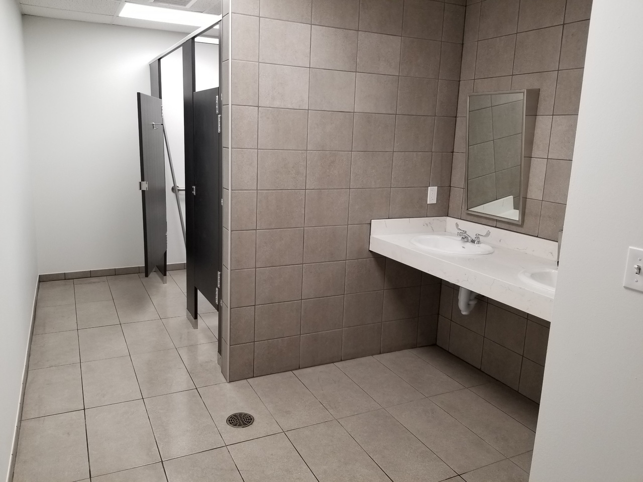 Photo of commercial restroom remodel. Shows tile flooring and walls with new sink and bathroom stalls.